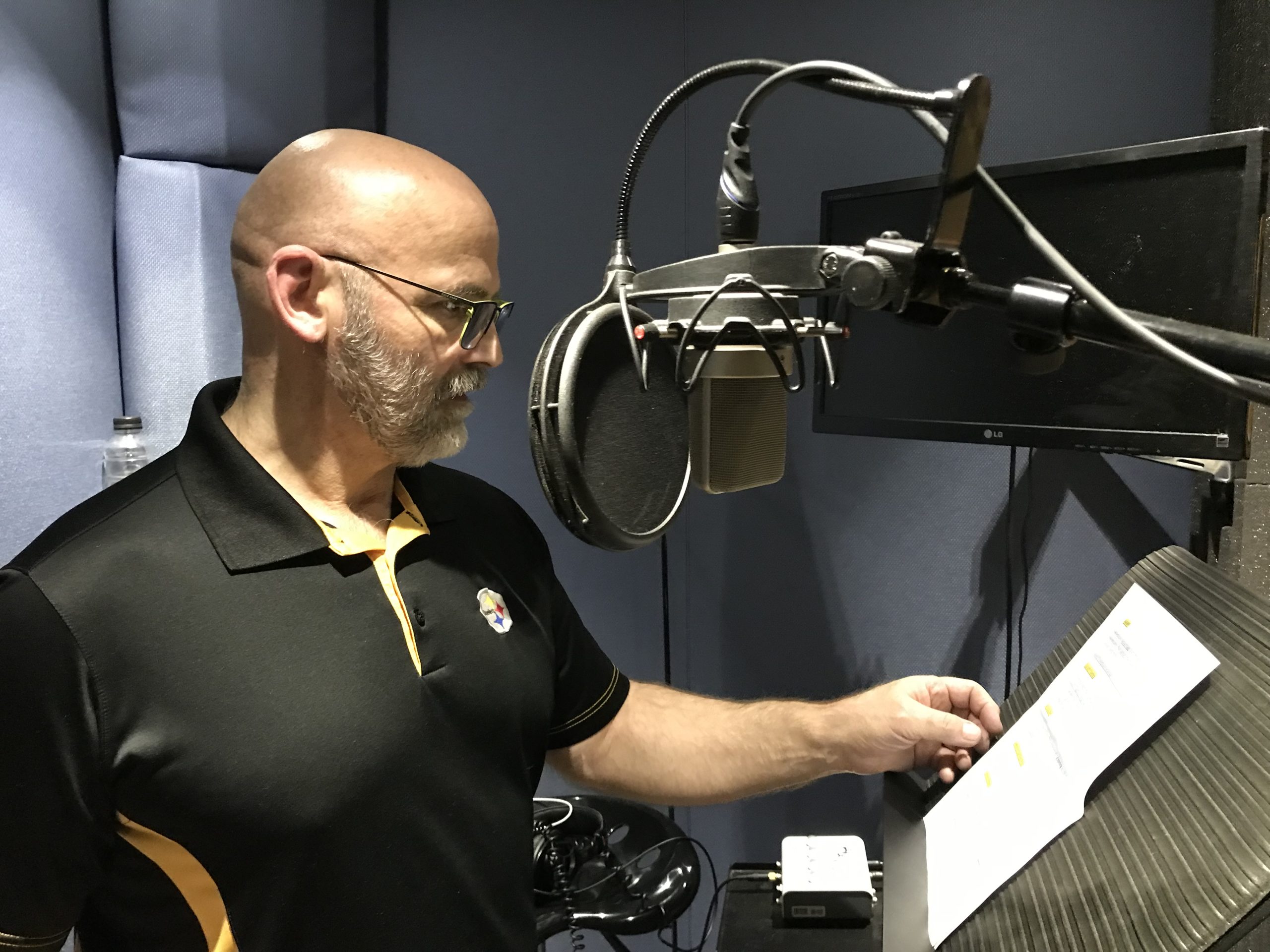 Marco Rigazio standing in front of a microphone wearing a black Pittsburgh Steelers polo shirt. Many Voices Media
